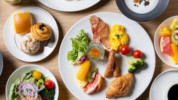 A variety of breakfast dishes including eggs, bacon, sausages, croissants, and fresh fruits on plates.