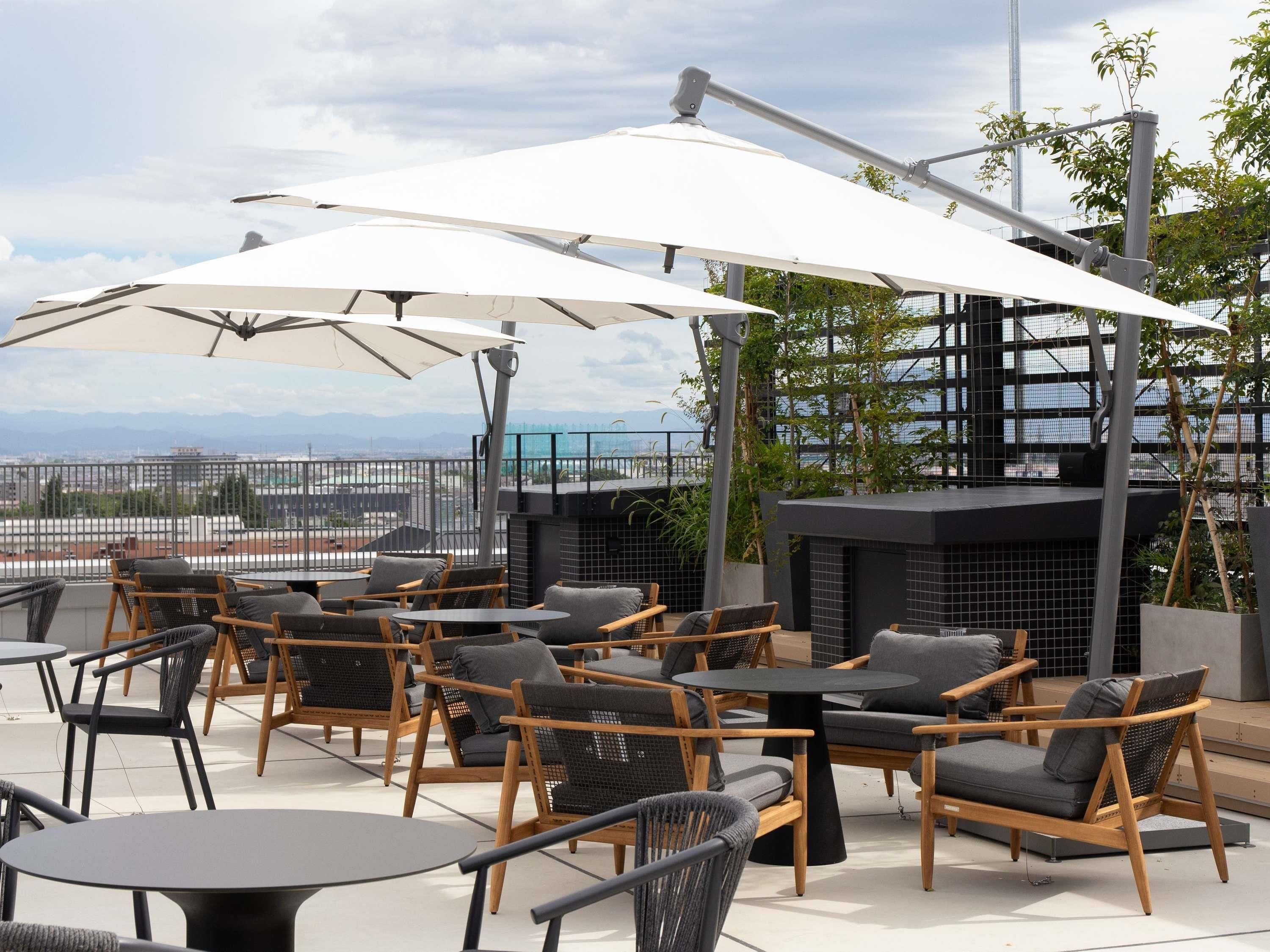 Un espace extérieur aménagé avec des tables, des chaises, des parasols et une vue sur le paysage urbain.