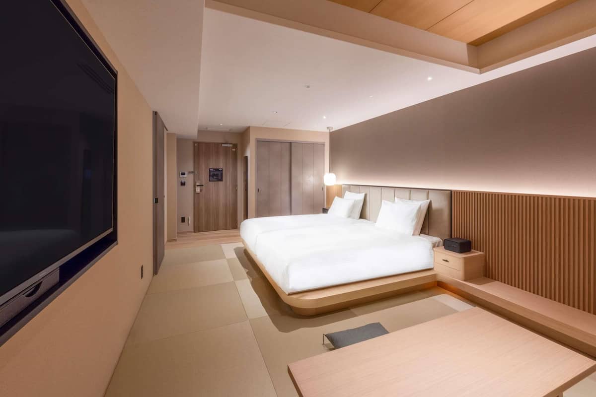 A modern hotel room with a large bed, a flat-screen TV, and a wooden headboard.