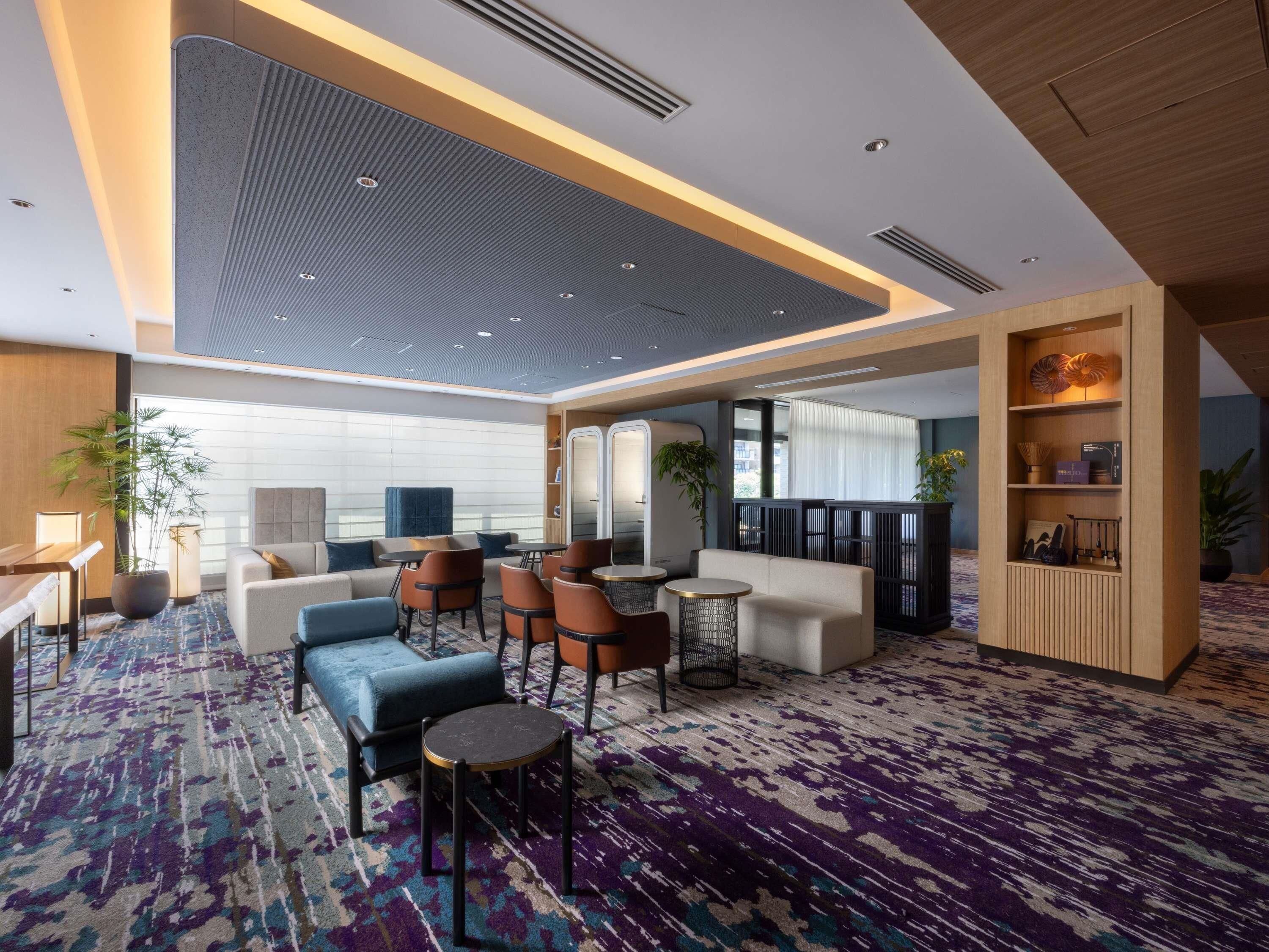 A modern hotel lobby with seating areas, a reception desk, and a decorative wall.