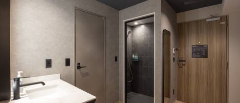 A modern bathroom with a sink, a shower, and a wooden door.