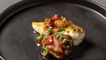 Un plat composé d’un champignon farci, de sauce tomate et d’herbes, le tout servi dans une assiette noire.