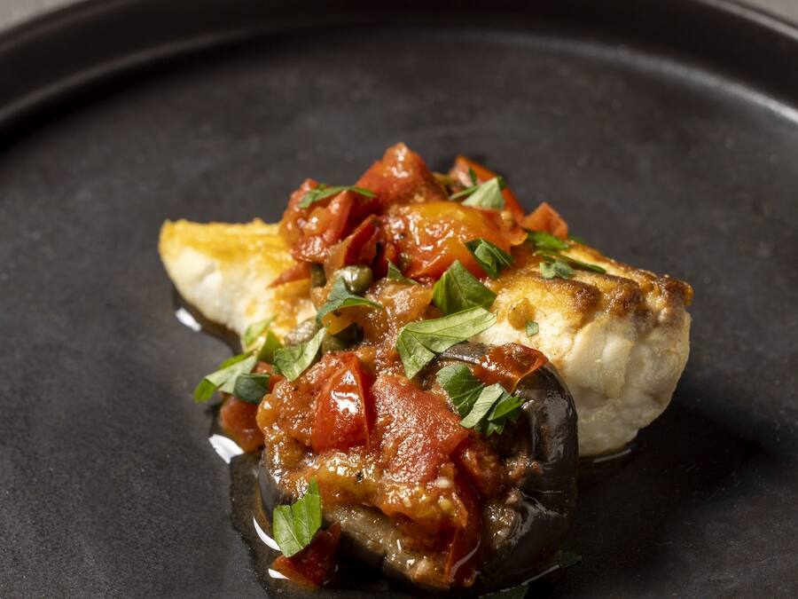 Un plat composé d’un champignon farci, de sauce tomate et d’herbes, le tout servi dans une assiette noire.