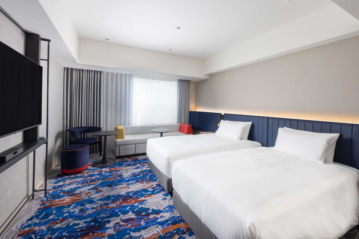 A hotel room with two beds, a TV, a desk, and a sofa.