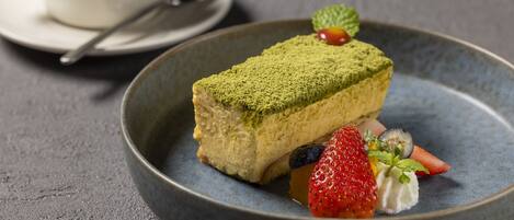 Une assiette à dessert avec une part de gâteau recouverte d’une poudre verte, accompagnée d’une fraise, d’un kiwi et d’une feuille de menthe.