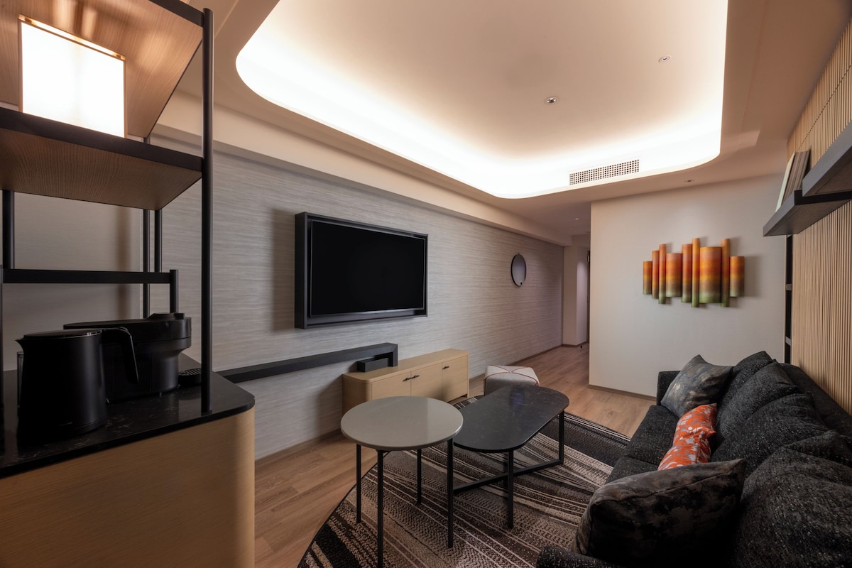 A modern living room with a flat-screen TV, a coffee machine, a small table, and a sofa with cushions.