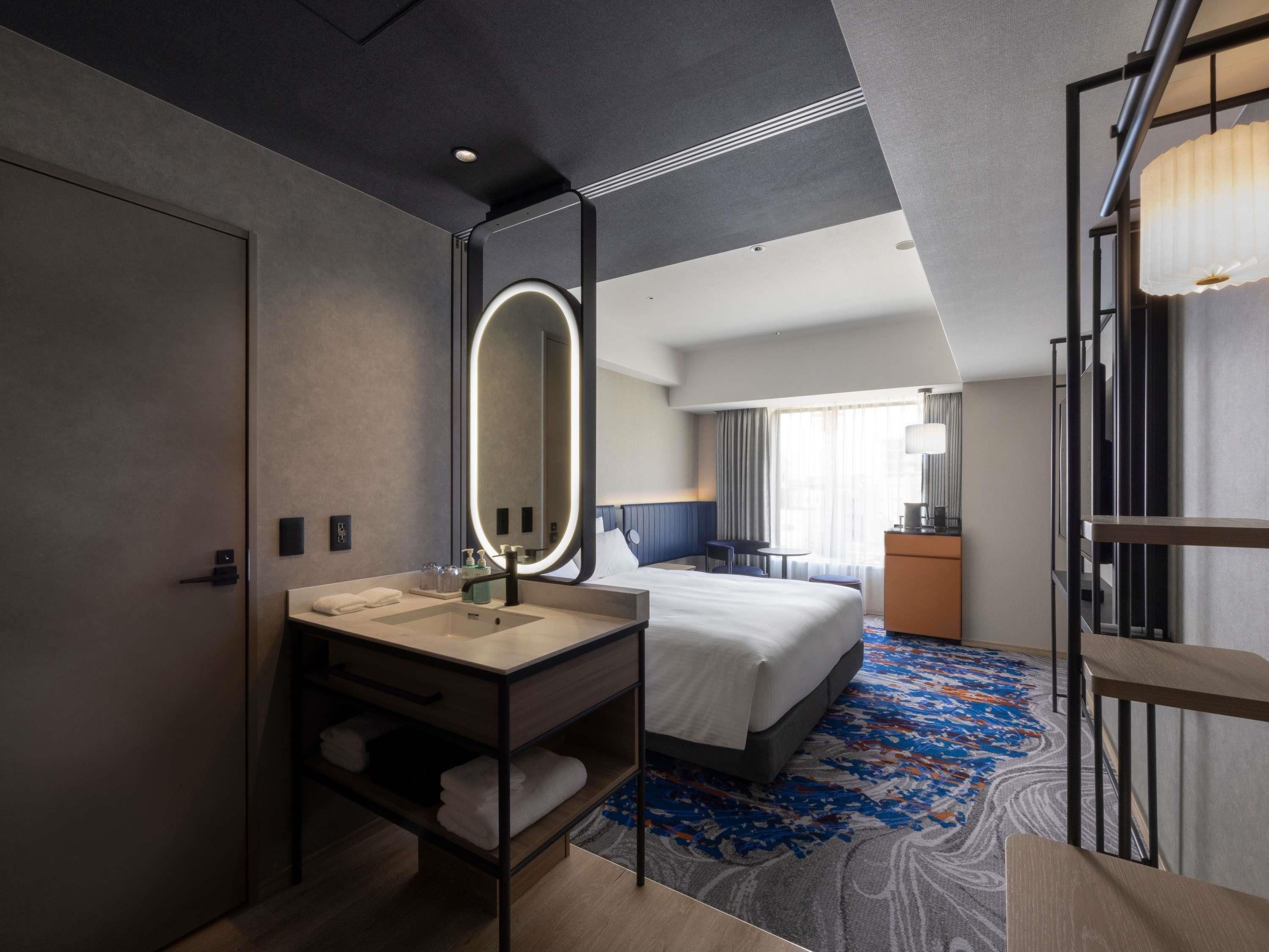 Ein modernes Hotelzimmer mit einem großen Bett, einem Badezimmer mit Spiegel und Waschbecken sowie Blick auf die Stadt.