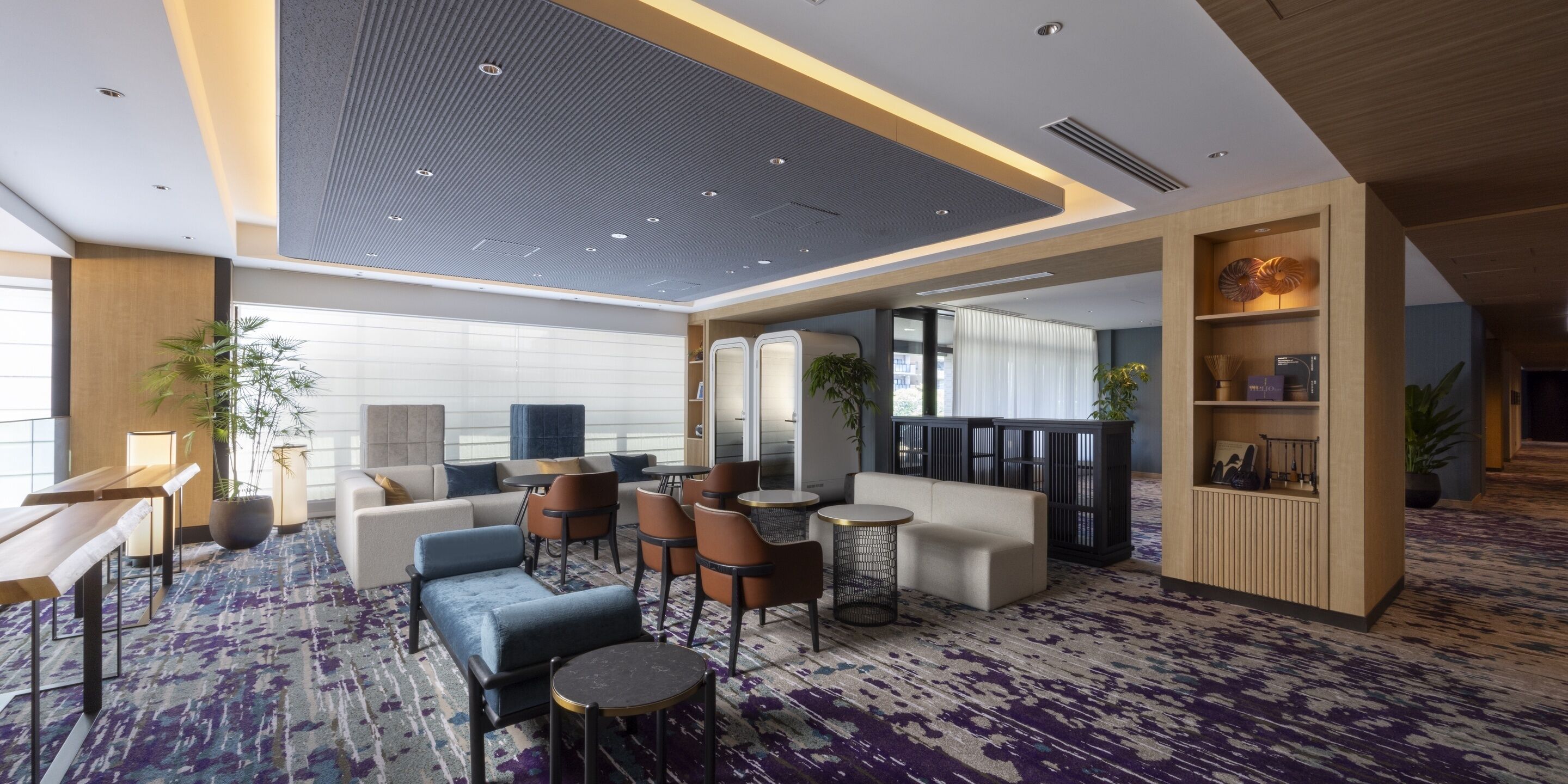 A modern hotel lobby with seating areas, a reception desk, and a decorative wall.