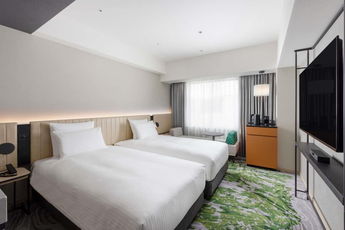 A hotel room with two beds, a desk, a TV, and a small table.