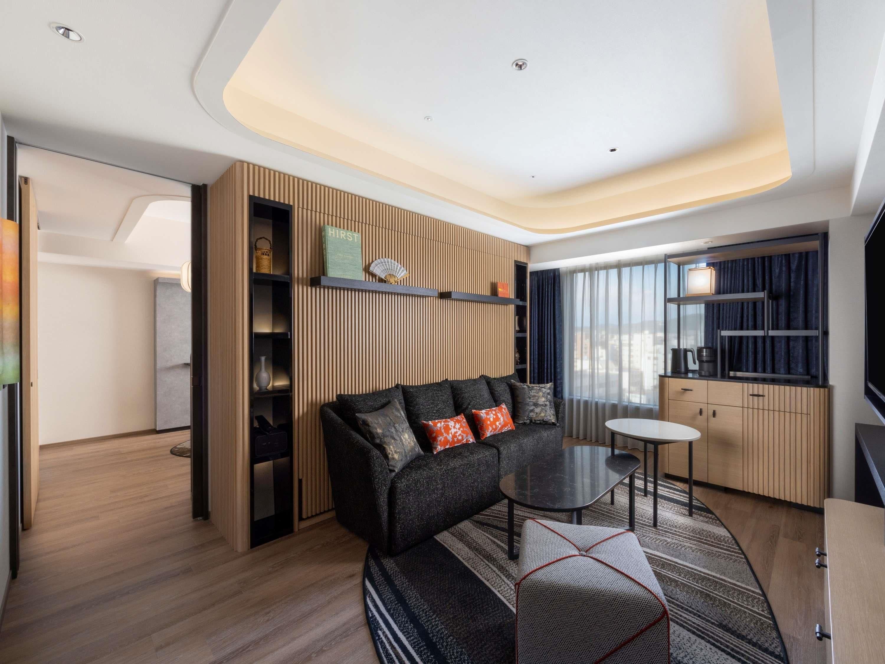 A modern living room with a sofa, a small table, and a kitchen area with a window.