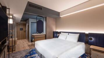 Una habitación de hotel moderna con una cama grande, televisión, escritorio con espejo y armario.