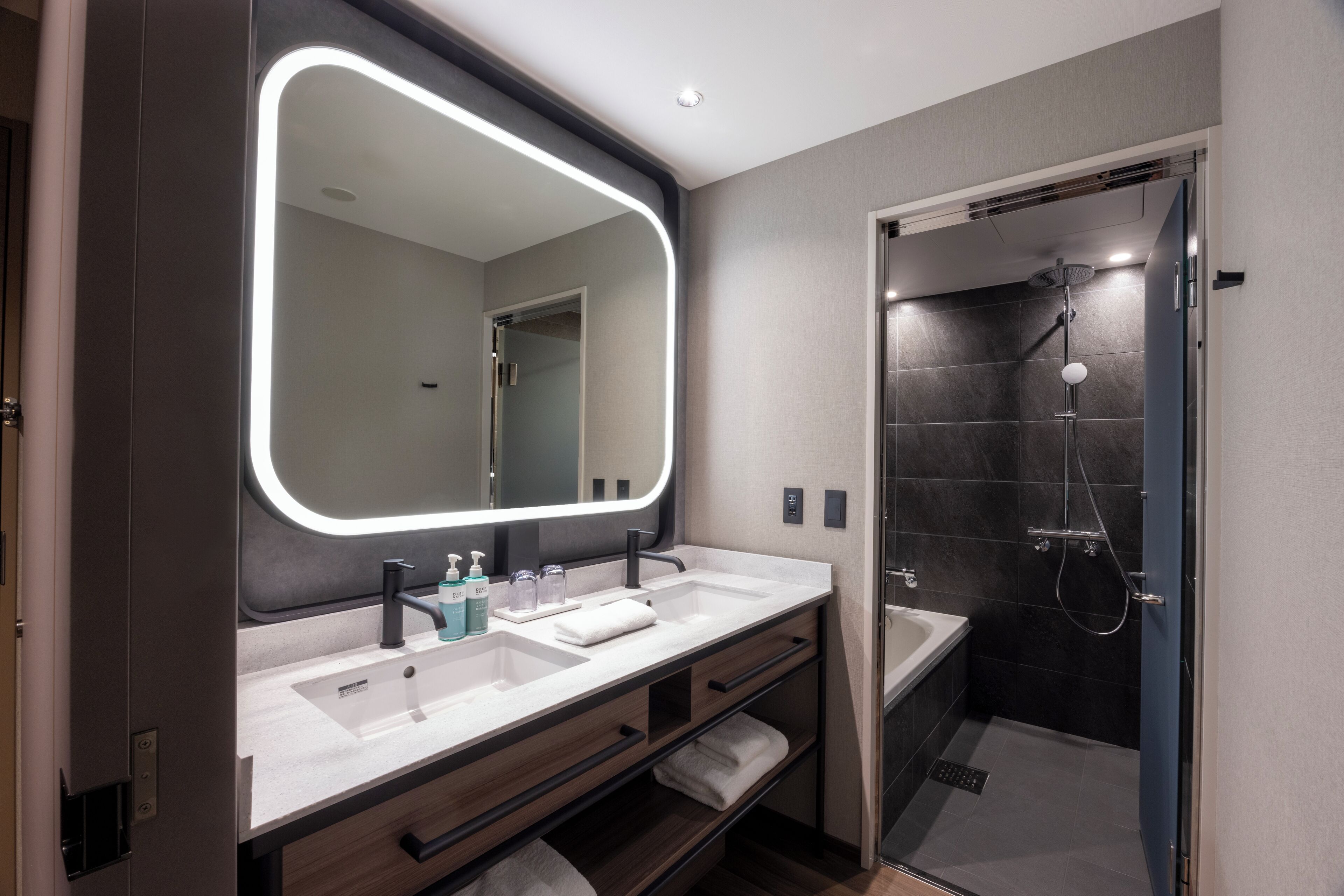A modern bathroom with a large mirror, dual sinks, and a walk-in shower.