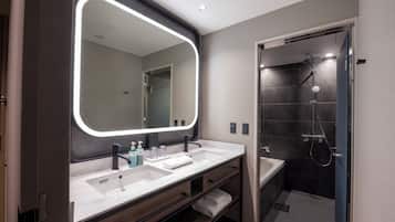A modern bathroom with a large mirror, dual sinks, and a walk-in shower.
