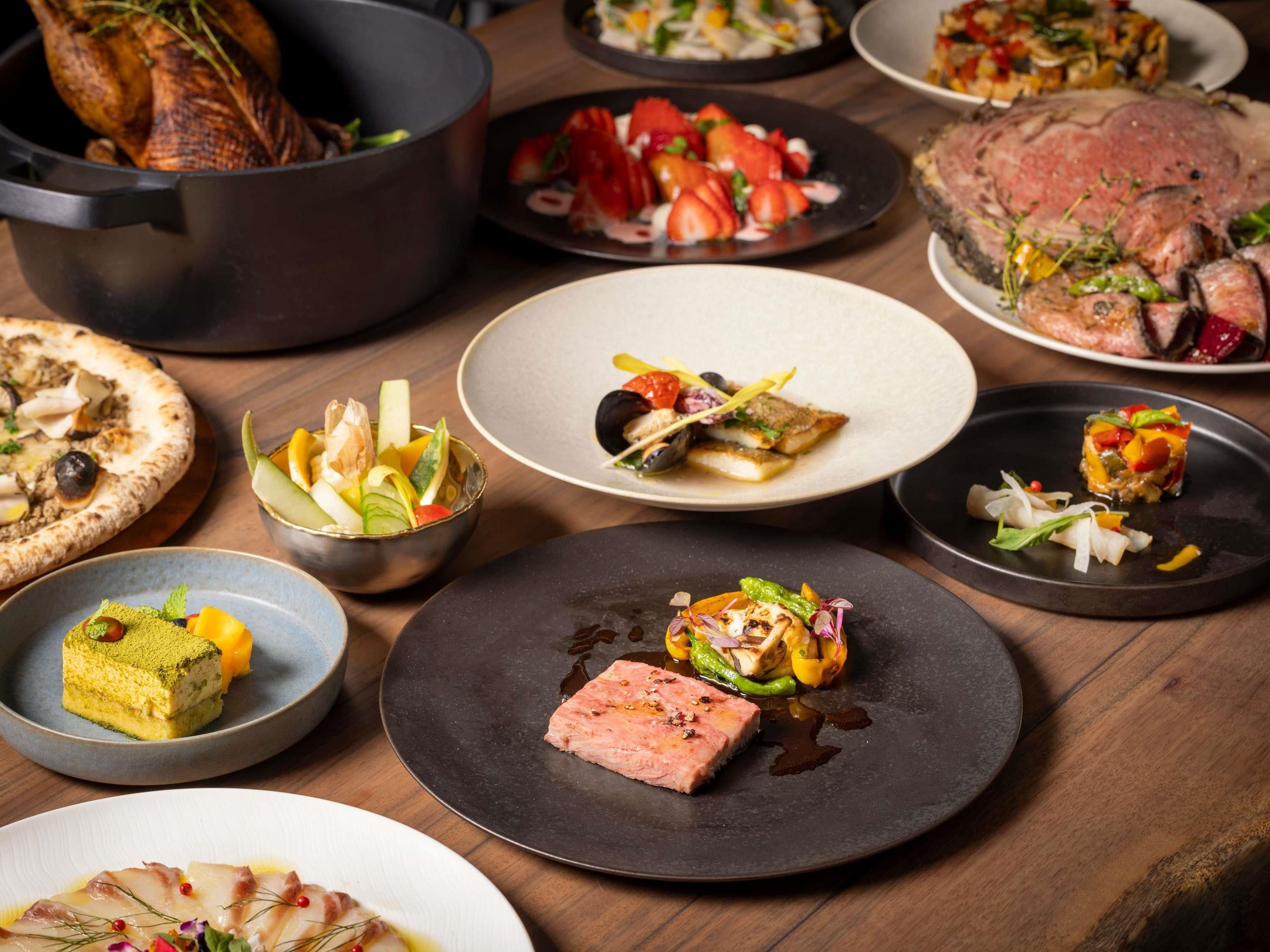 A variety of dishes on a wooden table, including a roasted turkey, steak, and several salads.