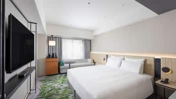 Habitación de hotel con una cama grande, un televisor de pantalla plana, una pequeña zona de estar y un escritorio con lámpara.