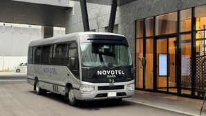 A Novotel NARA HINO bus parked outside a building with a modern facade and large windows. - Novotel Nara (Nara)
