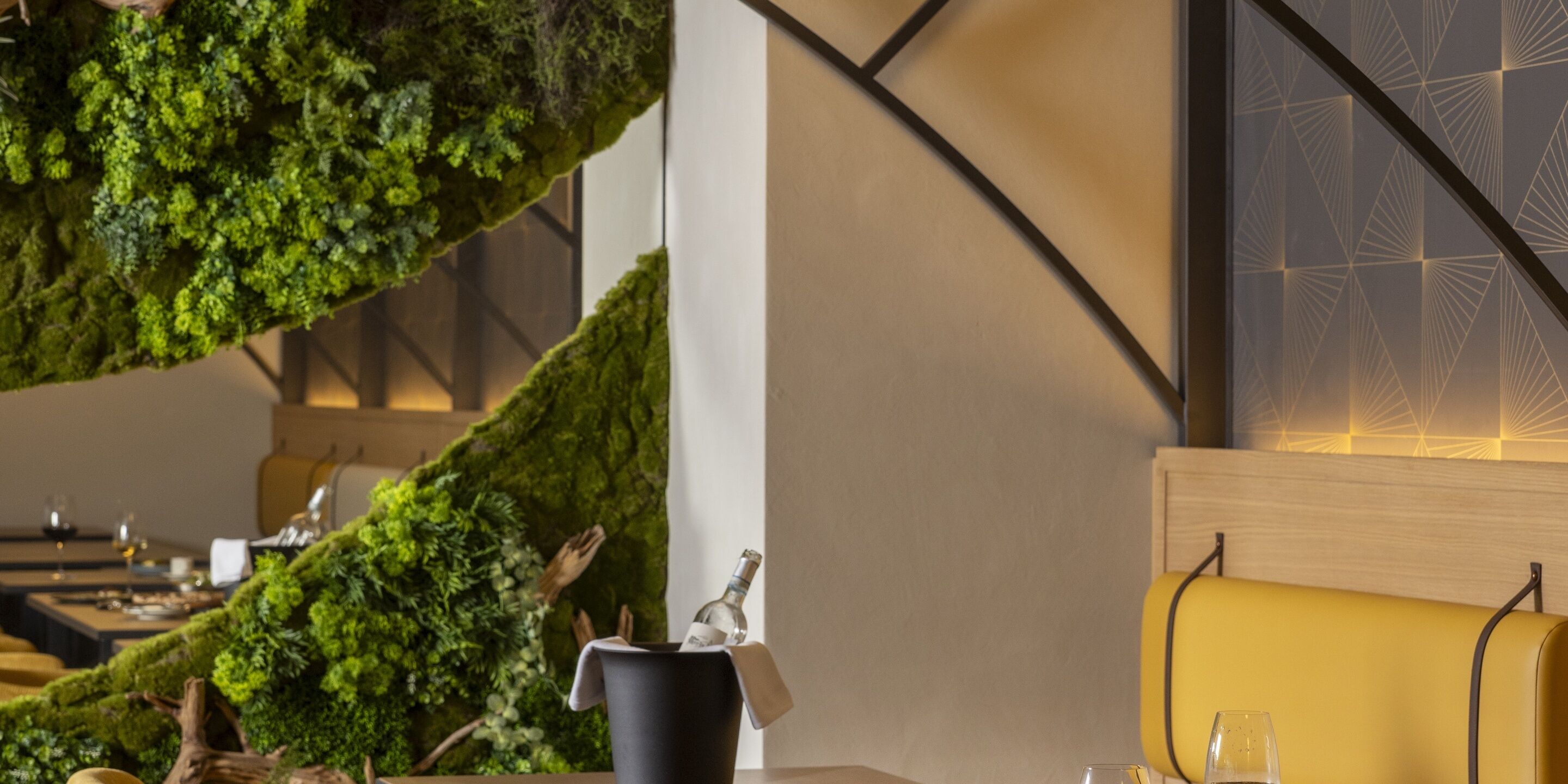 A restaurant interior with a moss-covered wall, a wooden table, and a yellow cushioned bench.