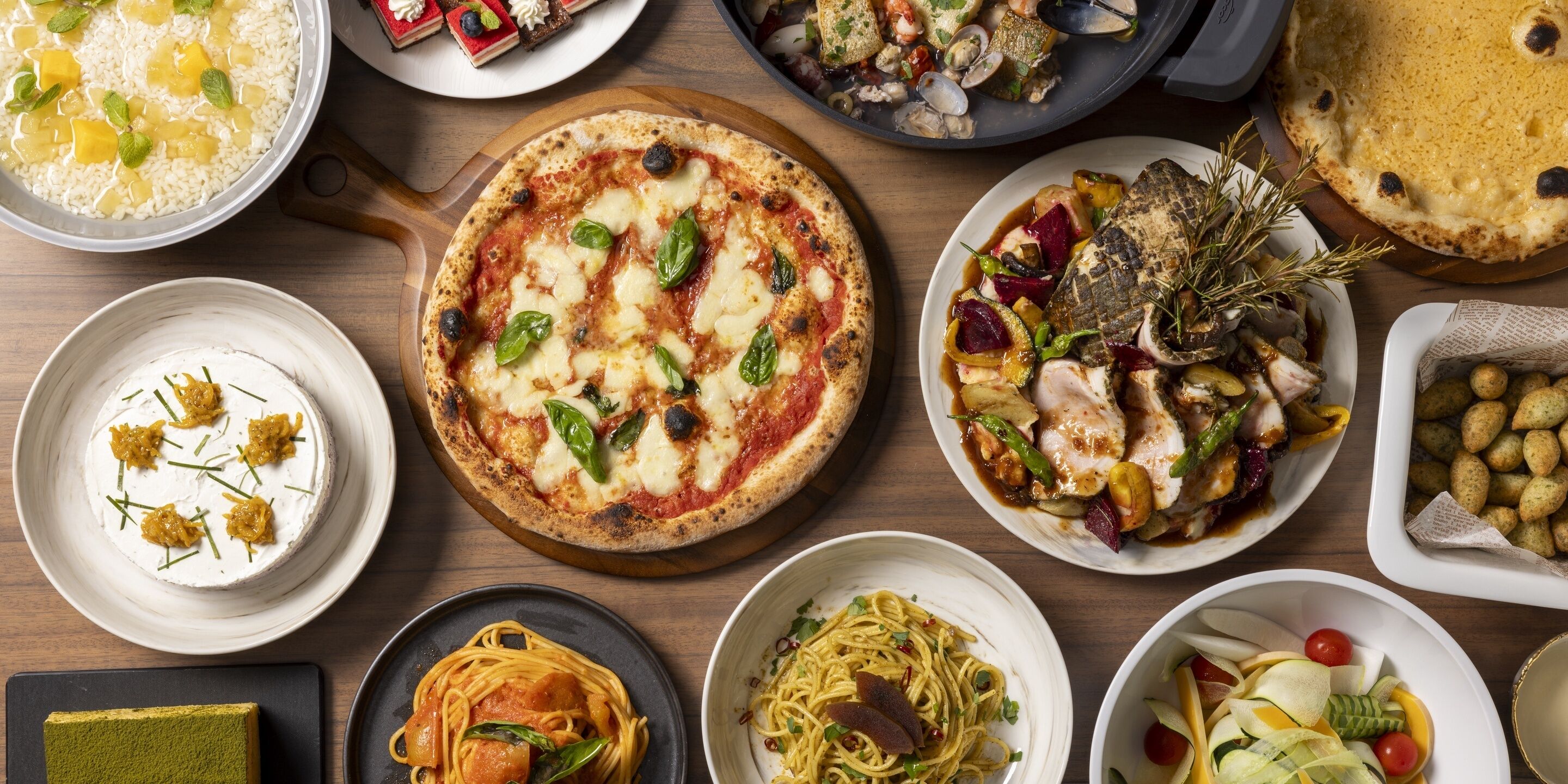 Diverse gerechten, waaronder pizza, pasta en zeevruchten, gepresenteerd op een houten tafel.
