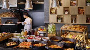 Un chef prépare des plats dans une cuisine équipée d’un four à bois, de différents postes de préparation et d’un buffet proposant un assortiment de plats et de condiments.