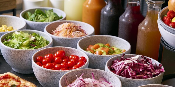 A variety of food bowls with different salads and a pizza slice.