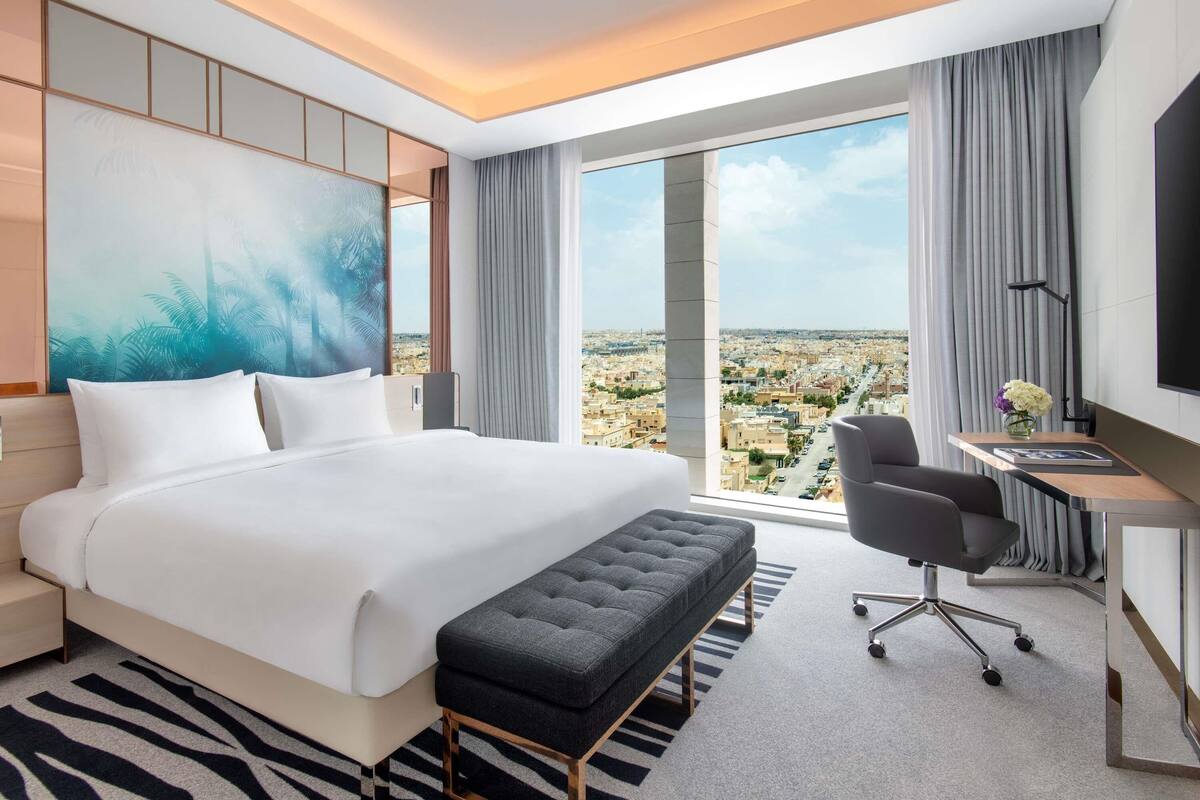 A hotel room with a large bed, a desk, a chair, and a view of the city.