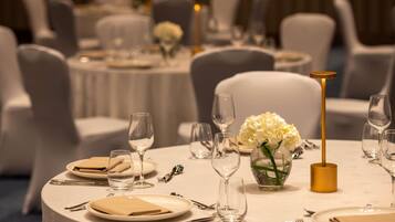 Une table ronde recouverte d’une nappe blanche, un vase avec des fleurs blanches et un chandelier doré.