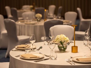 A round table with a white tablecloth, a vase with white flowers, and a gold candle holder.