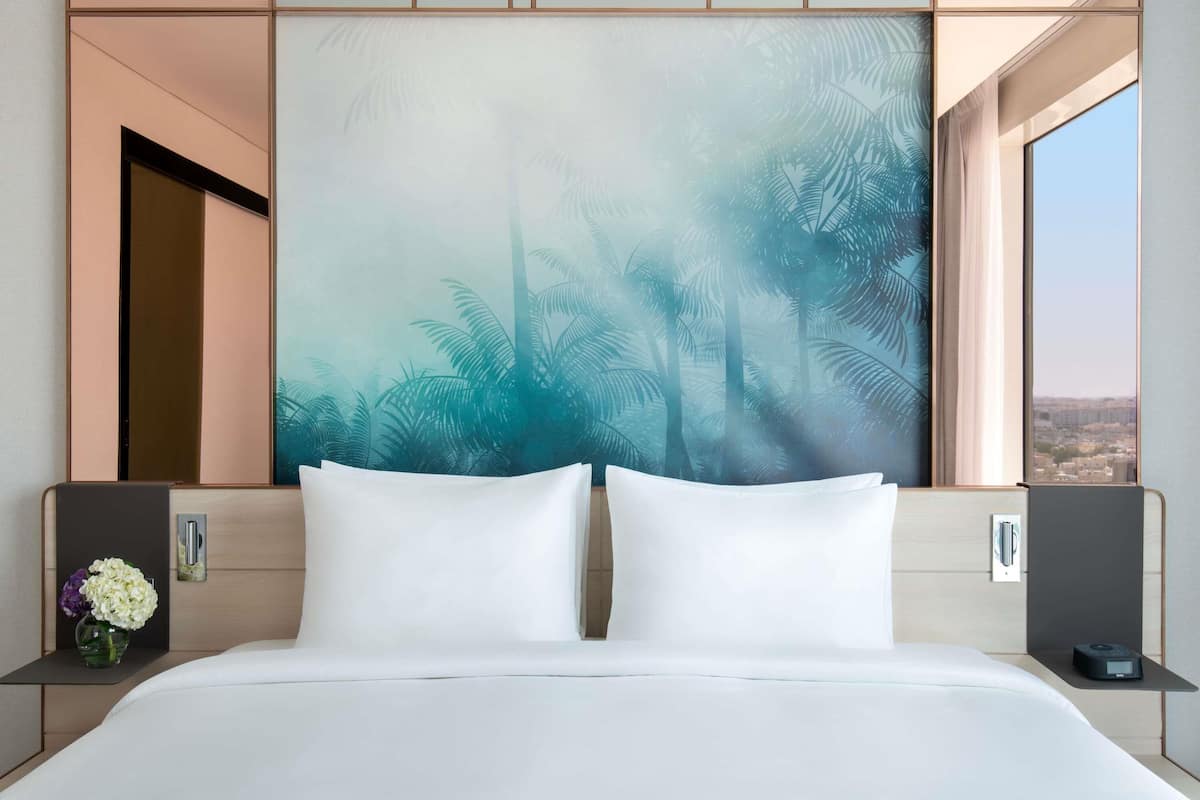 Habitación de hotel con una cama grande, vista a la ciudad y un mural temático tropical.