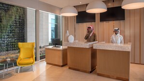 A reception area with two receptionists, a yellow chair, a large screen, and a wall with a vertical garden. - Novotel Riyadh Sahafa (Riyadh)