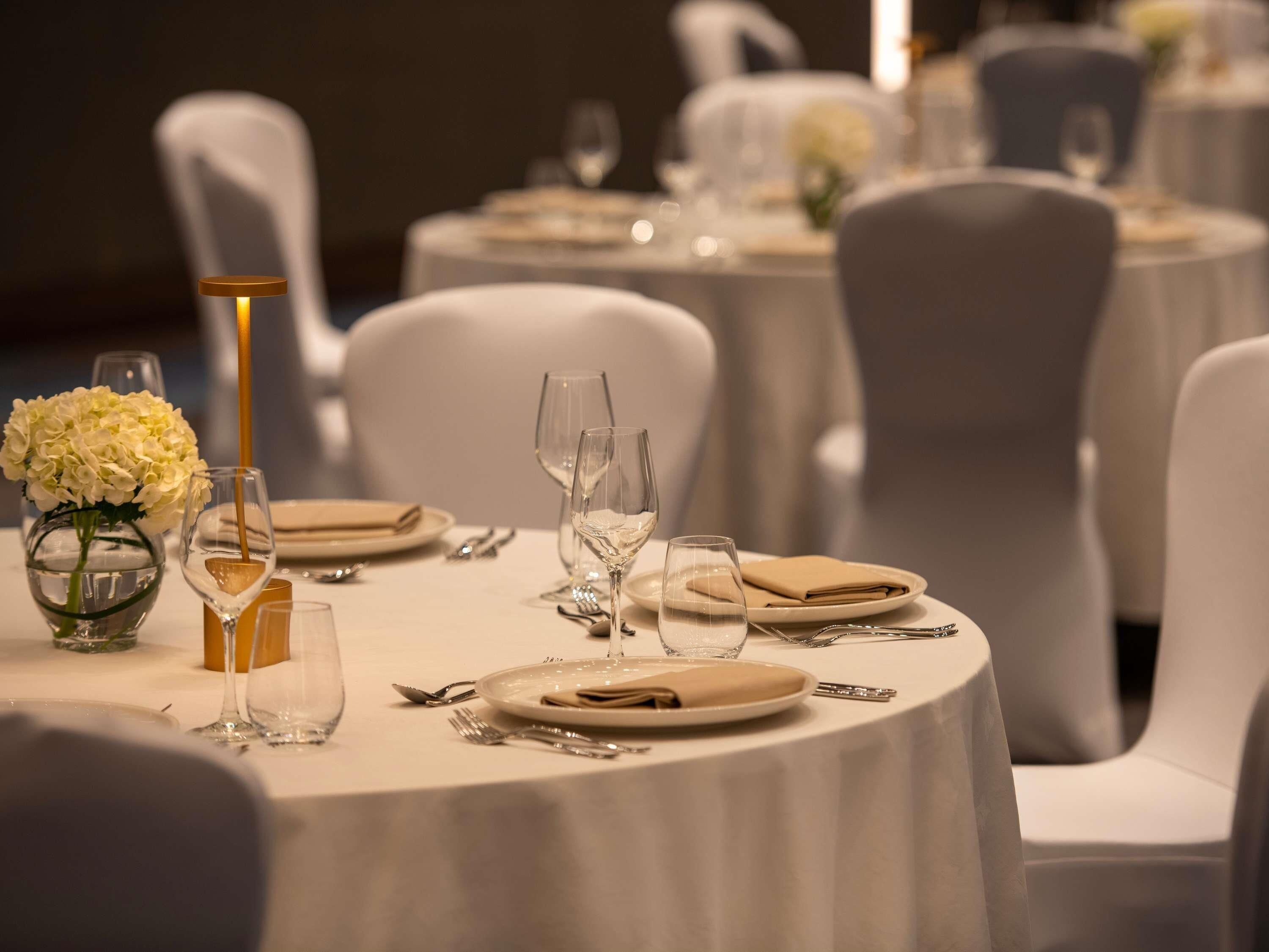 A dining table set with plates, cutlery, and glasses, surrounded by white chairs.