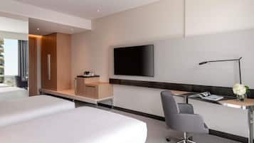 A modern hotel room with a bed, desk, chair, TV, and a city view.