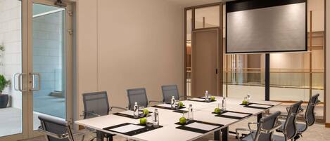 A conference room with a large table, chairs, a projector, and a screen.