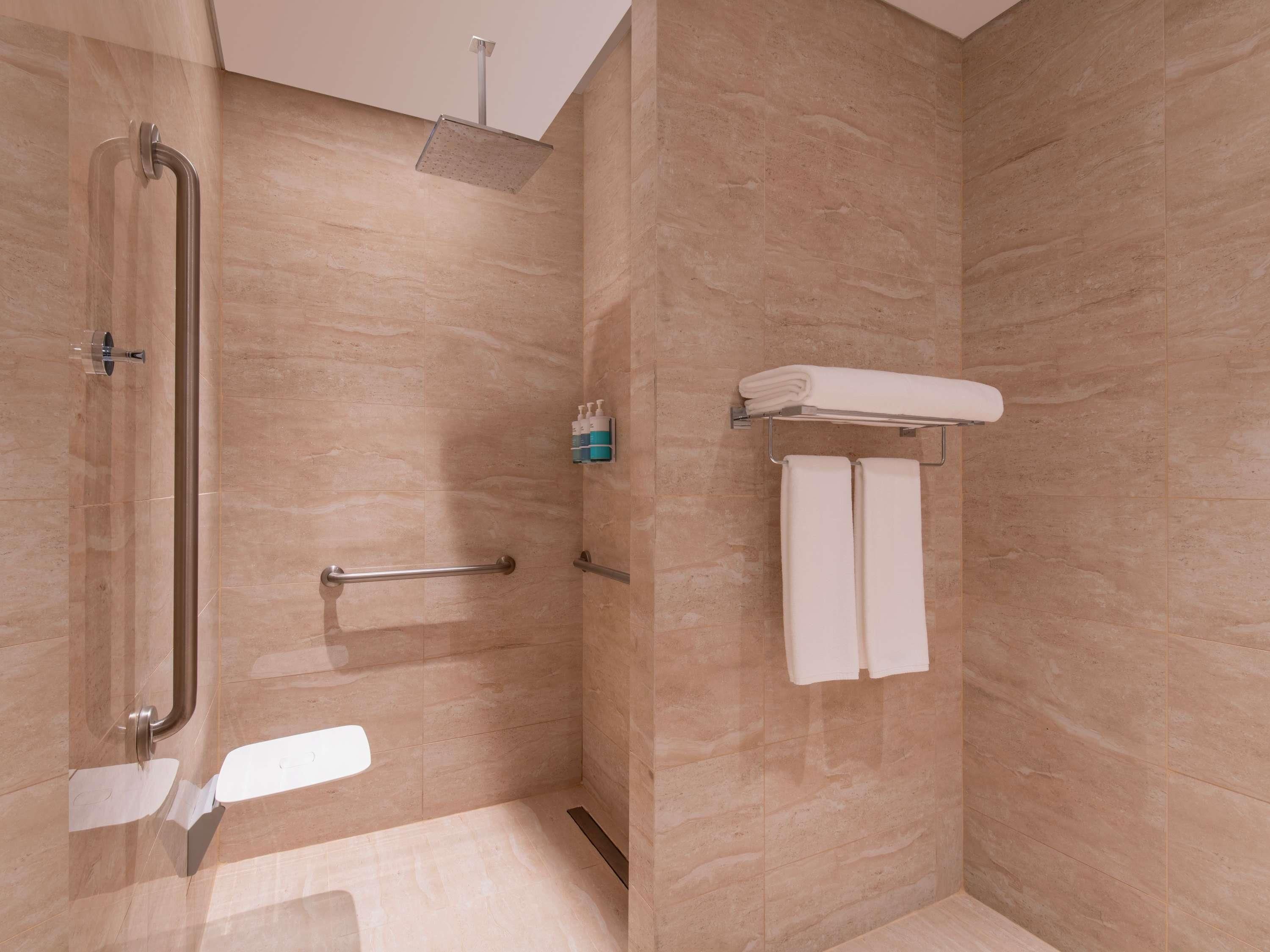 Un baño moderno con ducha, barras de apoyo, un perchero para toallas y un dispensador de papel higiénico.