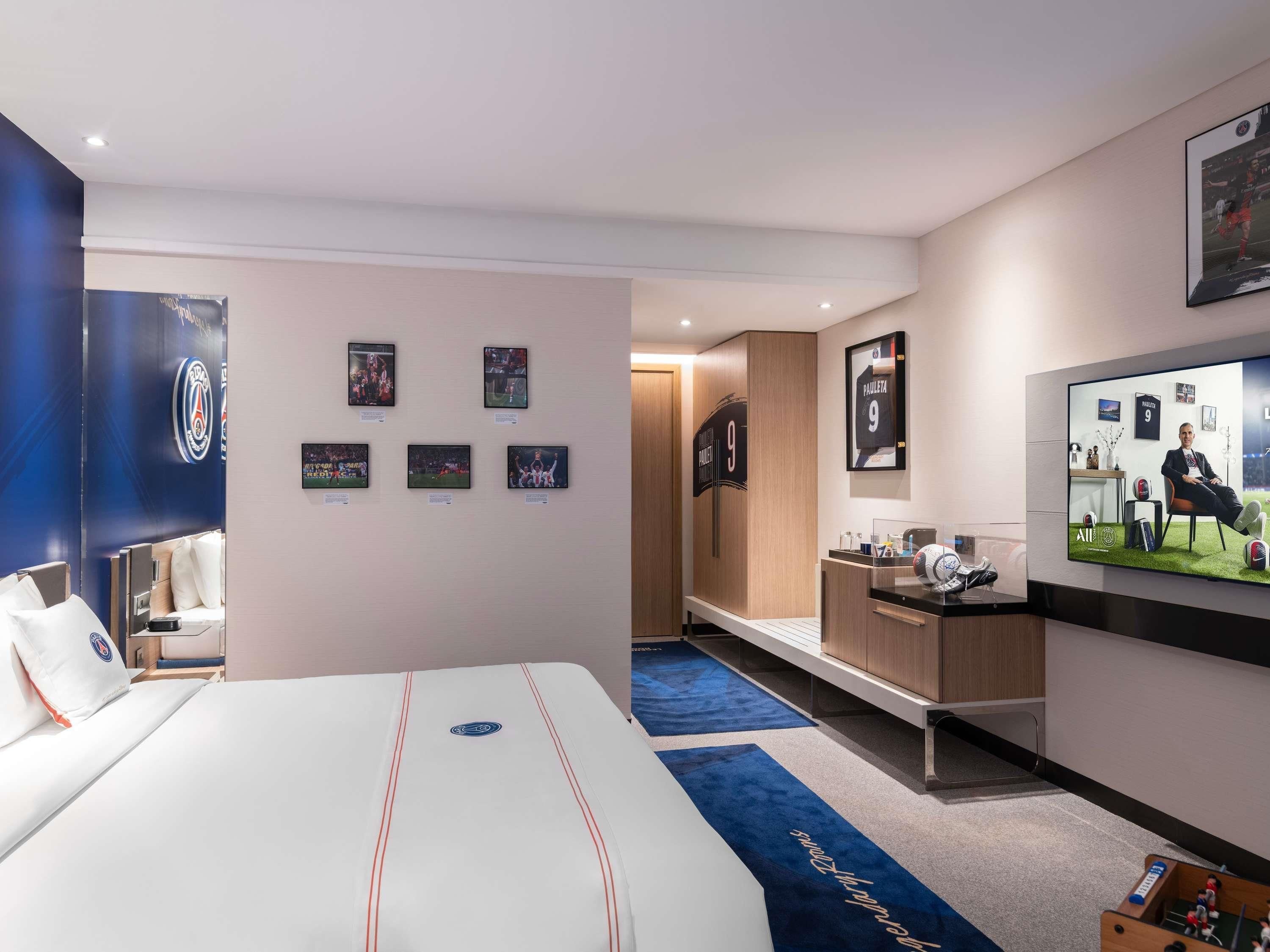 A hotel room with a bed, a desk, a TV, and wall-mounted pictures.