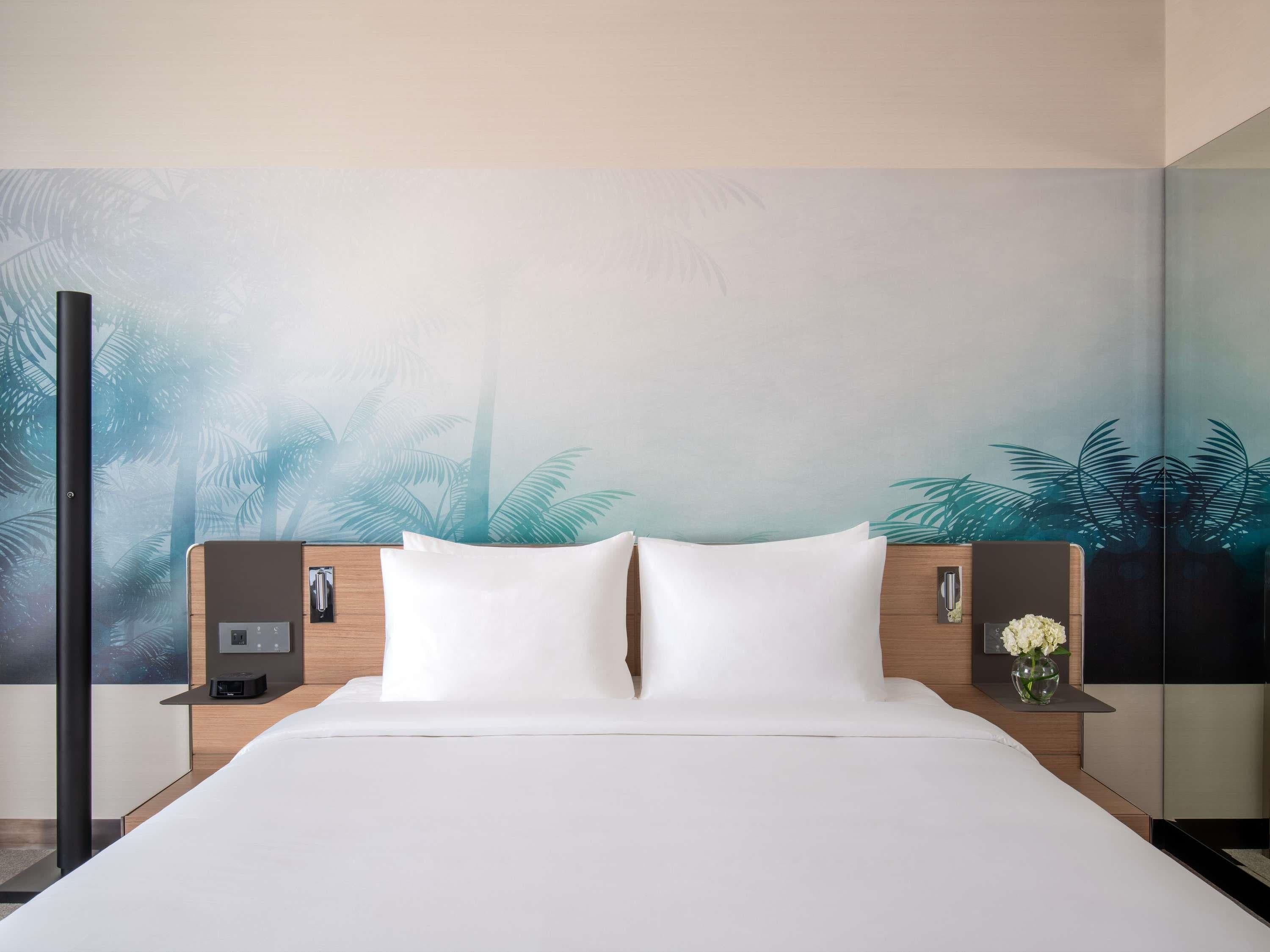 A hotel room with a large bed, two bedside tables, a nightstand, and a wall mural.