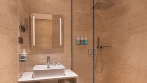 A modern bathroom with a glass-enclosed shower, a white sink with a mirror above it, and toiletries on the wall.