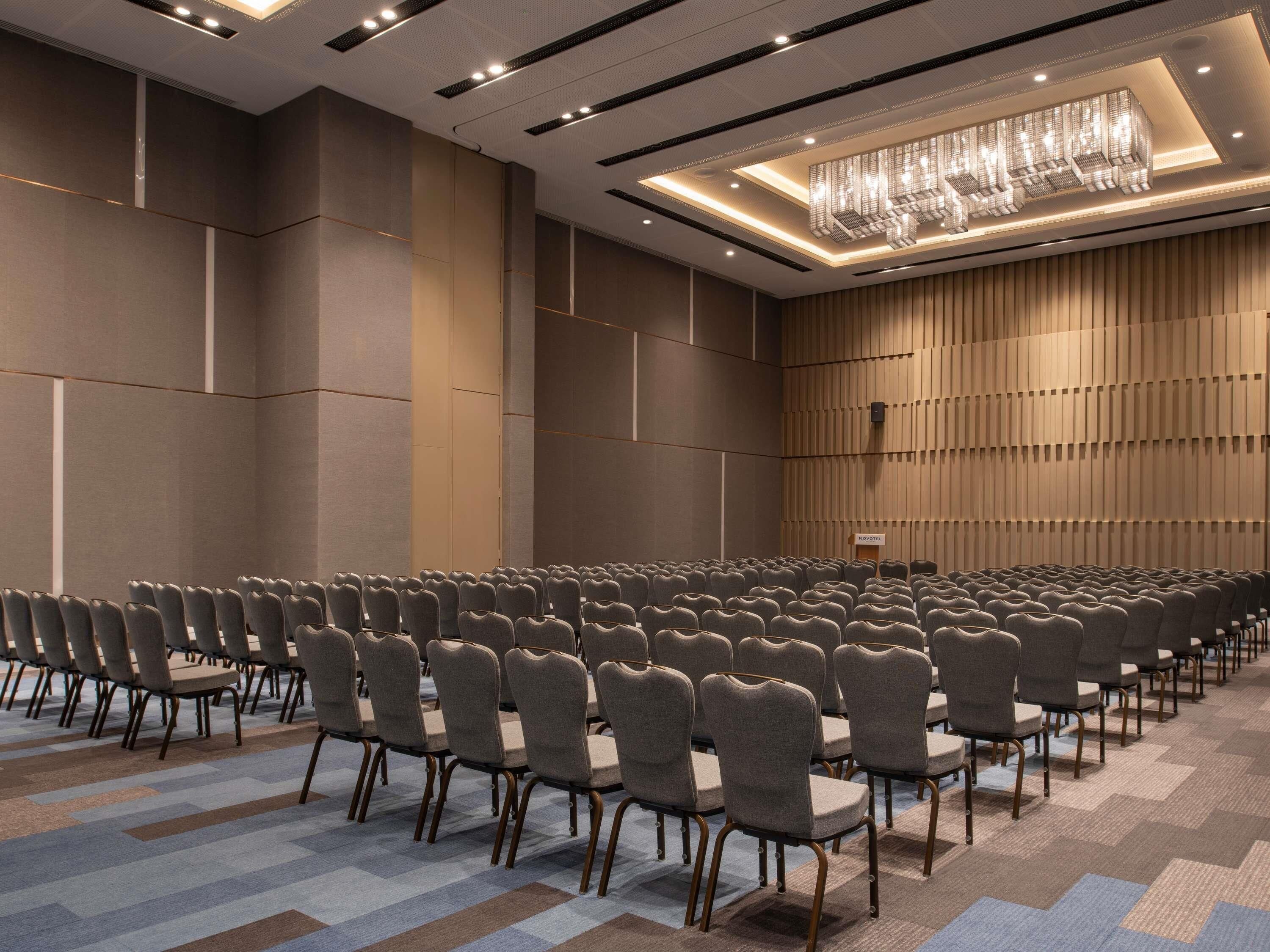 Une salle de conférence avec des rangées de chaises, un pupitre et une moquette à motifs.