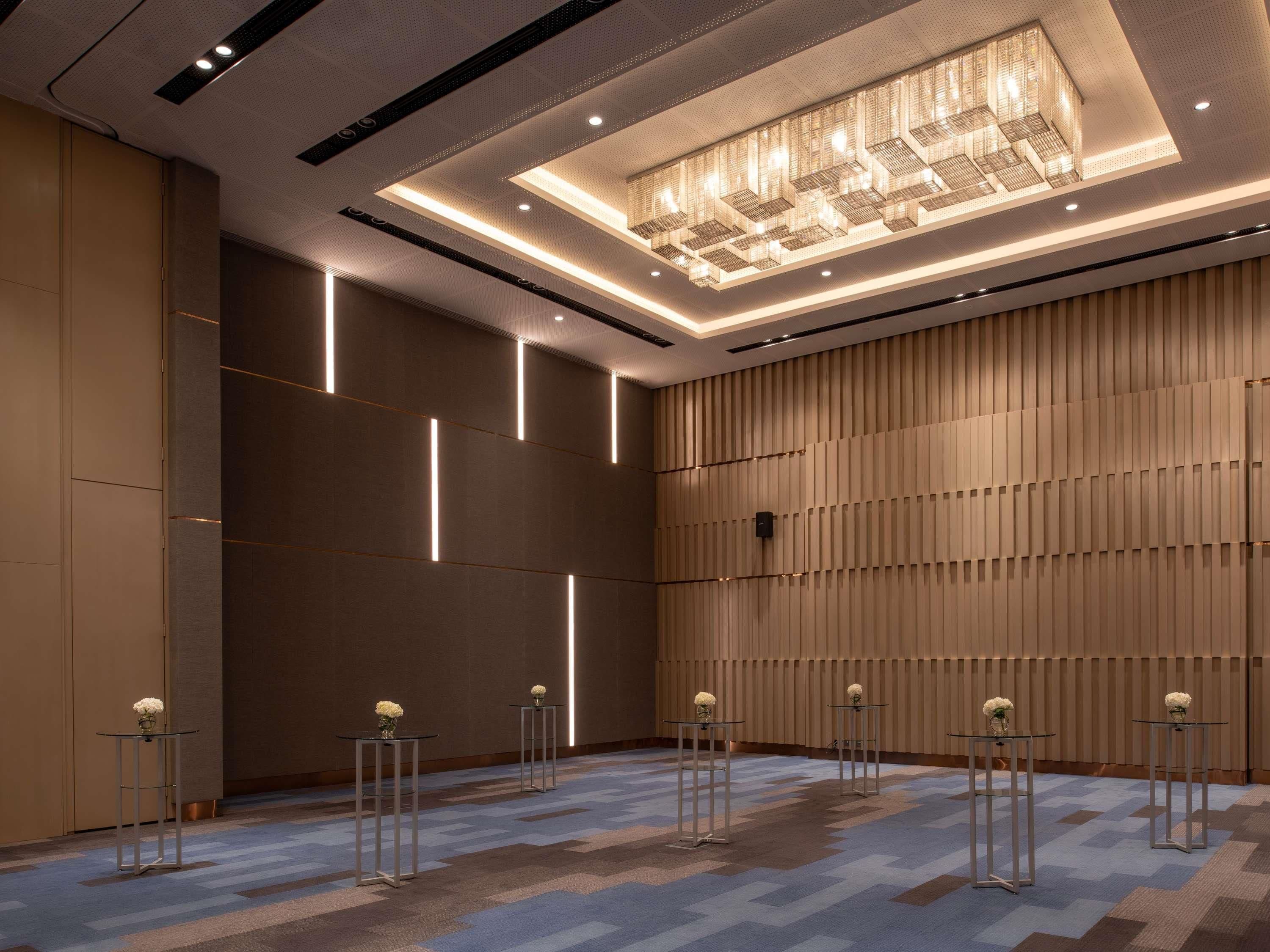 A modern hotel room with a geometric patterned carpet, recessed lighting, and a central chandelier.