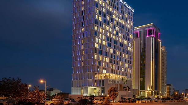A high-rise hotel with a grid-like facade, illuminated windows, and a prominent sign at the top.