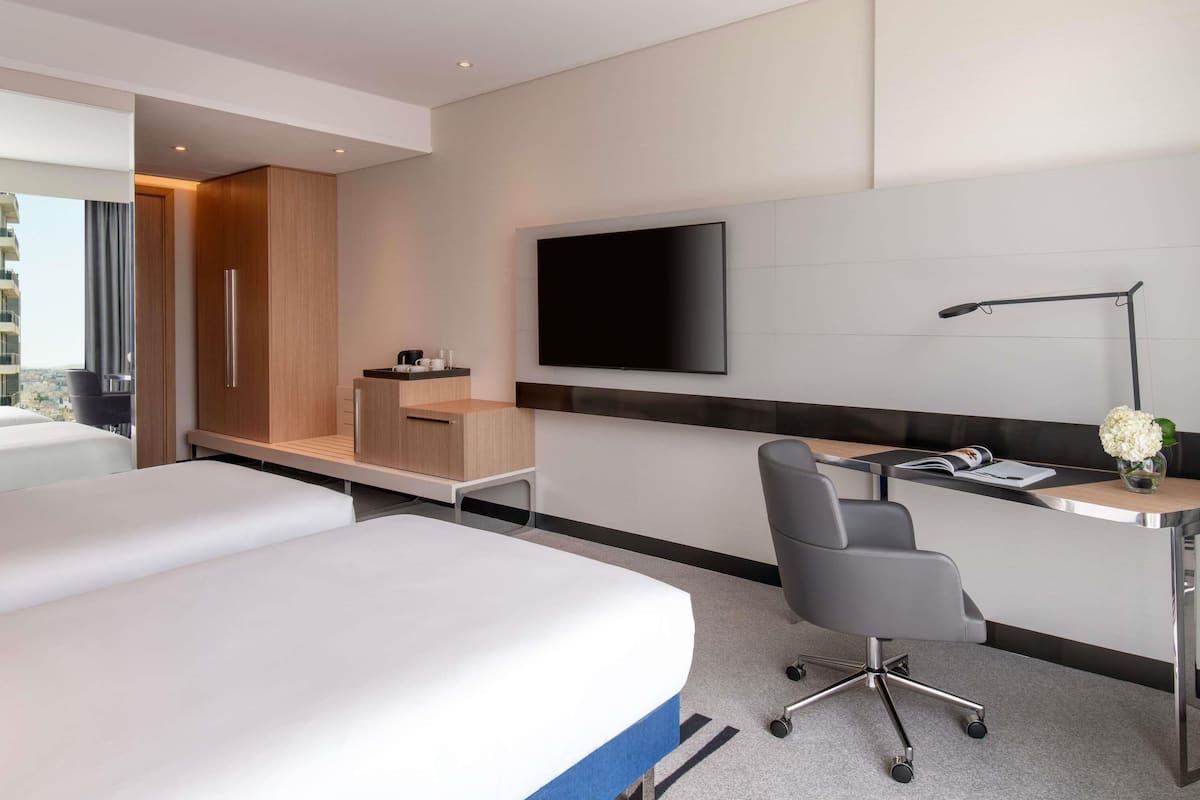 Una habitación de hotel moderna con cama, escritorio, silla, televisor y vistas a la ciudad.
