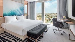 A hotel room with a large bed, a desk, a chair, and a view of the city.