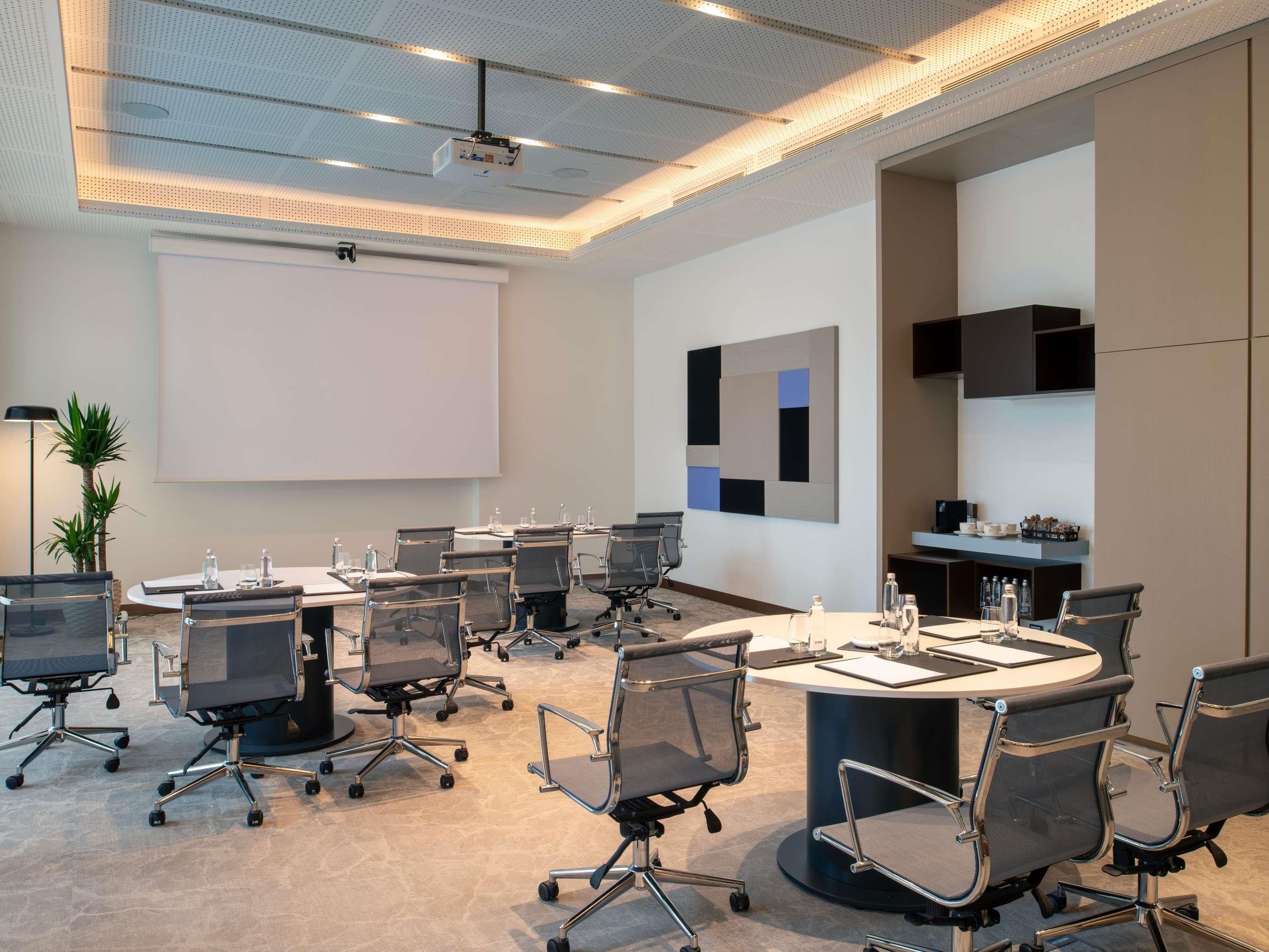 A conference room with a large screen, round tables, and modern chairs.