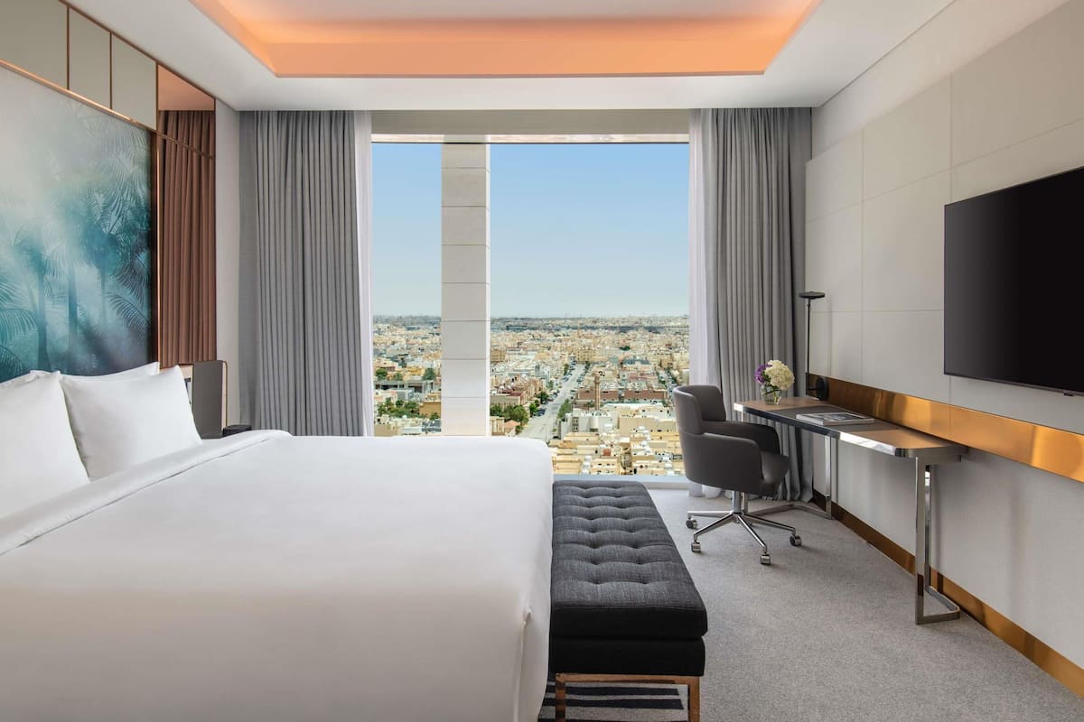 Habitación de hotel con una cama grande, un escritorio, una silla, un televisor y vistas a la ciudad.
