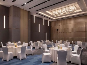 Un salón de banquetes con mesas redondas, sillas blancas y una araña de cristal.