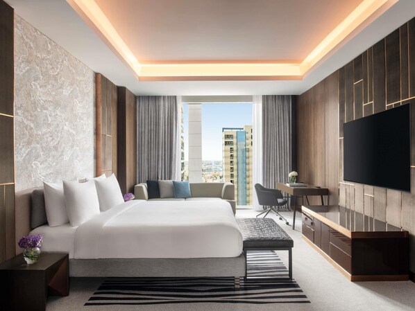 A modern hotel room with a large bed, a desk, a TV, and a view of the city. - Novotel Riyadh Sahafa (Riyadh)