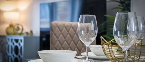 A dining table with a white bowl, two wine glasses, and a gold basket.