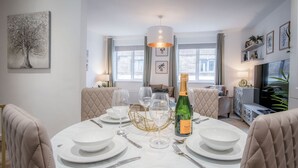 Un coin repas avec une table ronde dressée pour six personnes, une bouteille de champagne et un lustre.