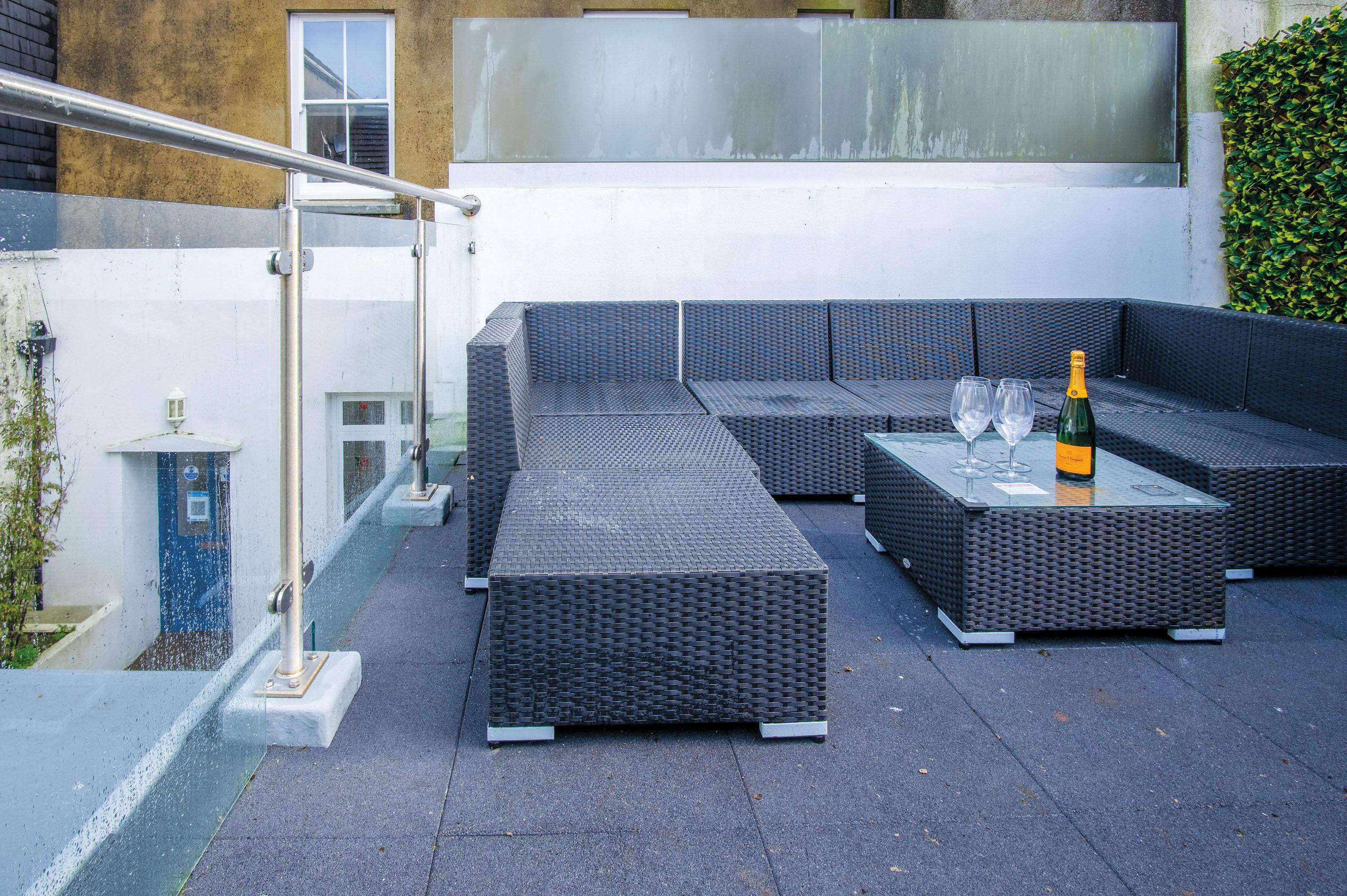 A rooftop patio with a sectional sofa and a table with two glasses and a bottle.