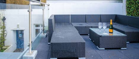 A rooftop patio with a sectional sofa and a table with two glasses and a bottle.