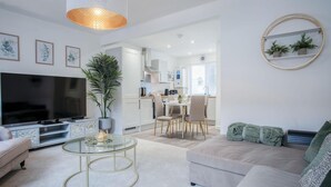 Un salon moderne doté d’un téléviseur à écran plat, d’une table basse en verre, d’un canapé beige et d’un coin repas avec une table et des chaises blanches.